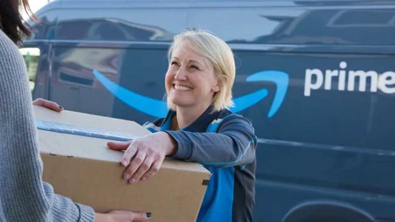 Woman delivering a package wearing a long-sleeved shirt in front of an Amazon Prime van.