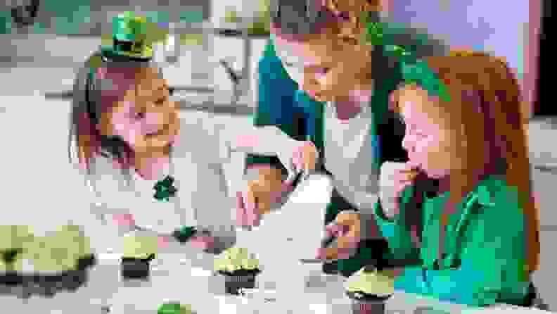 A parent helps two children make St. Patrick's Day cupcakes.