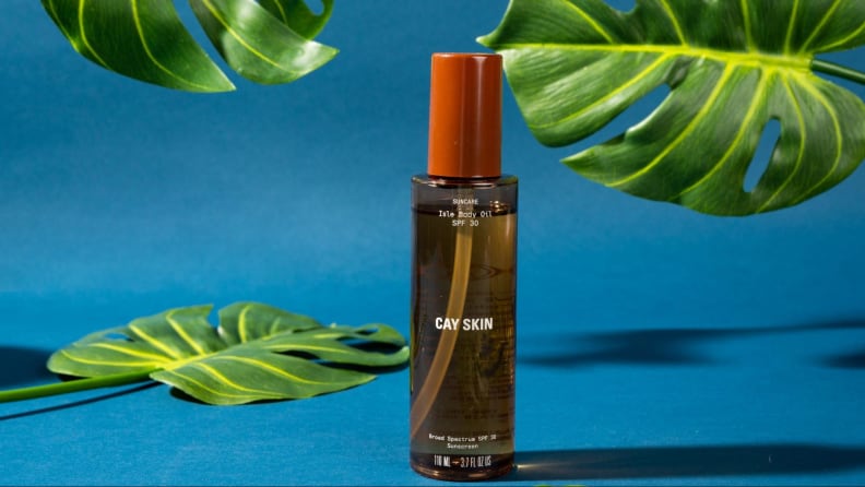 A bottle of sunscreen oil against a blue background and foliage.