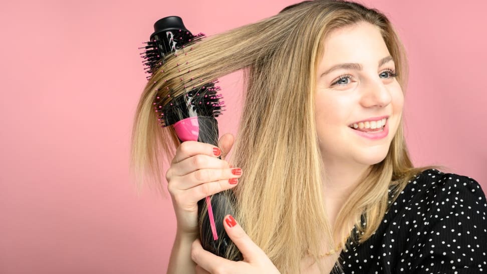 Woman doing hair with black and pink hair tool, against a pink background