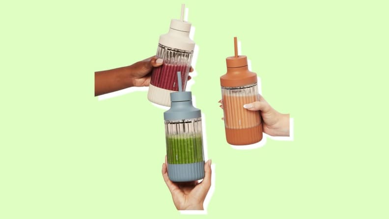 Three hands hold a white, orange and light blue Beast Blender Mini cup.