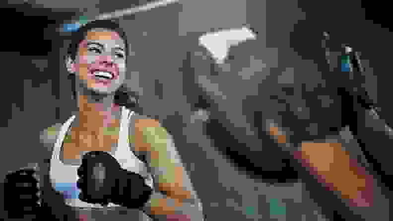 A woman smiling while exercising with a partner at a boxing gym.
