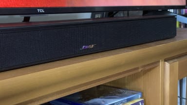 The Bose Smart Soundbar 600 on a wooden home theater credenza with a TCL TV behind it.