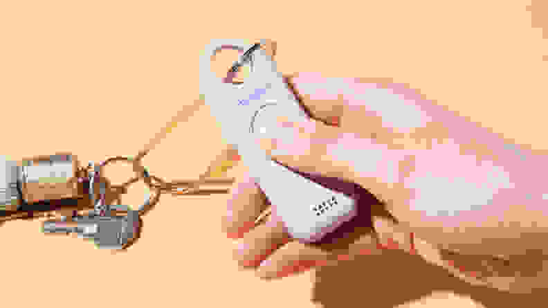 A person holding the She's Birdie+ with a keychain attached to it, on an orange background.