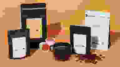 Four different bags of Lifeboost Coffee and a black coffee mug filled with Lifeboost Coffee on an orange background.