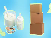 Powdered baby formula next to teething ring, baby bottle and three stacked shipping boxes.