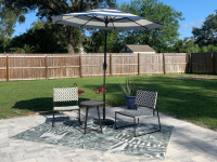 A patio set-up with an outdoor rug, two chairs, small table, and an umbrella.