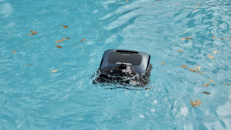 A black, square robot sucks up leaves floating in pool water