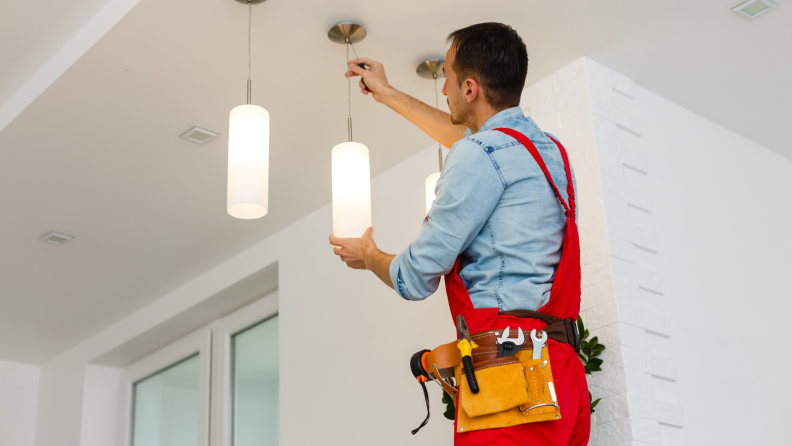 Electrician installing light fixture on ceiling.