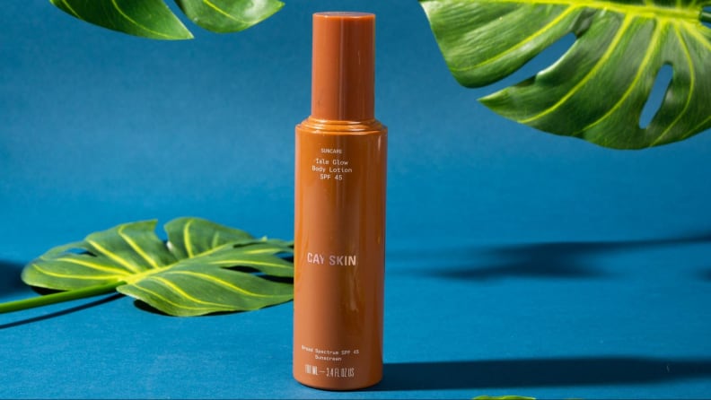 A tan bottle of face lotion against a blue background and foliage.