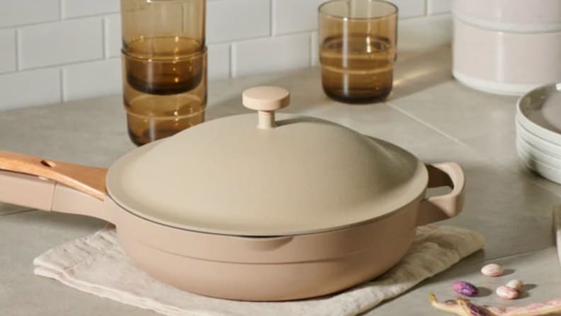 An image of a beige Our Place Always Pan on a countertop surrounded by amber glasses and napkins.