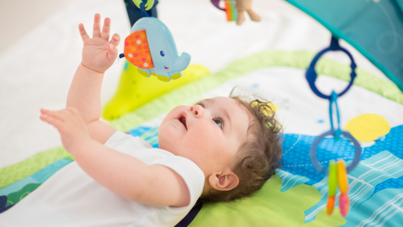 Small baby reaching upwards to play with hanging toys on swing.