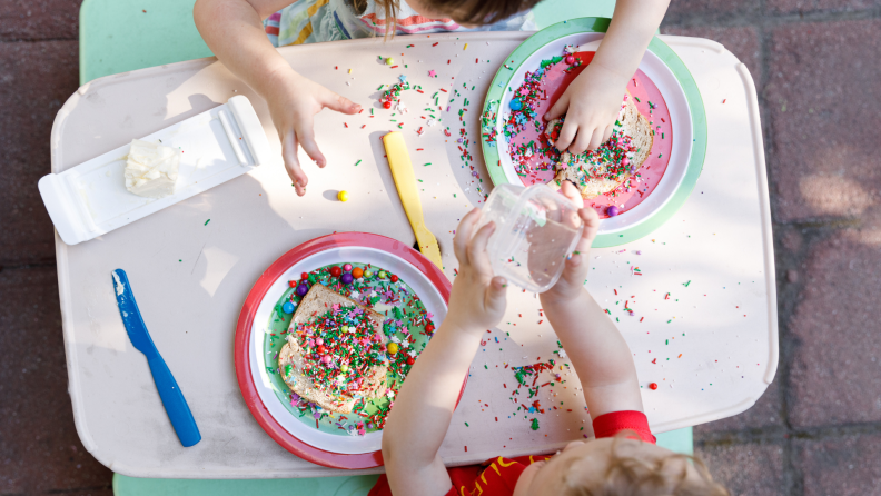 Young boy and girl playing together with multi-colored sprinkles on table in front of them.
