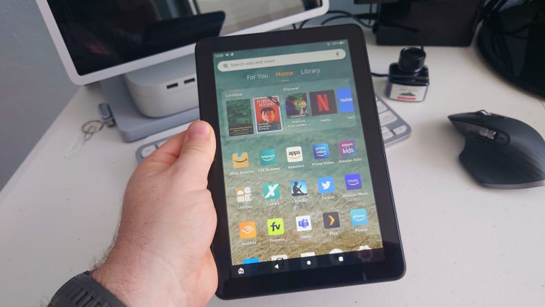 A man holds an Amazon Kindle Fire tablet while sitting at his desk