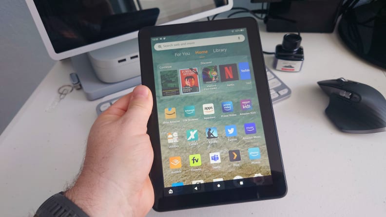 A person is holding an Amazon Kindle Fire tablet while sitting at a desk