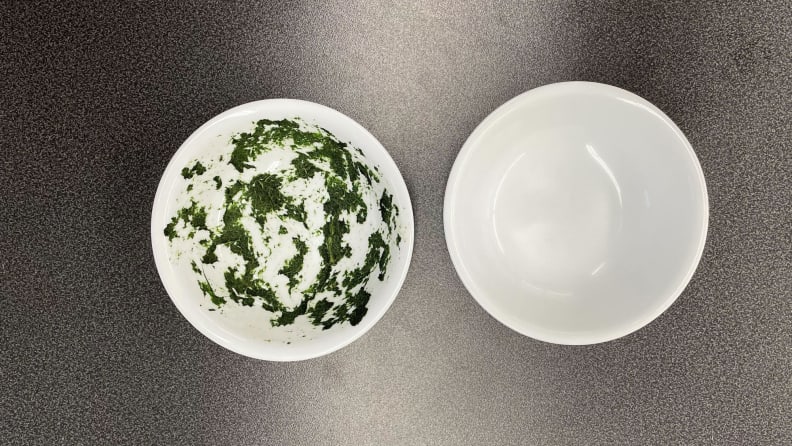 A dirty bowl with green food in side the bowl and a clean bowl to it.