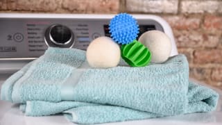 Four different brands of the best dryer balls are photographed atop a couple soft blue towels on the lid of a dryer.
