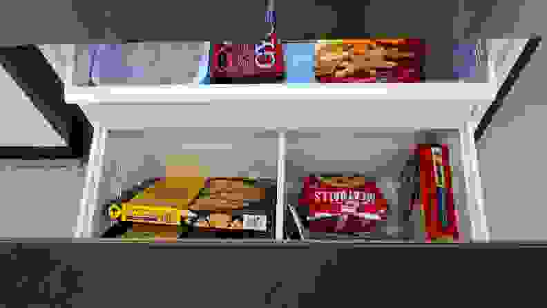 A close-up of the fridge's open freezer drawer, showcasing its main bin and the shelf that sits above it. The left corner of the upper shelf houses an ice reservoir. The rest of the space is filled with frozen foods.