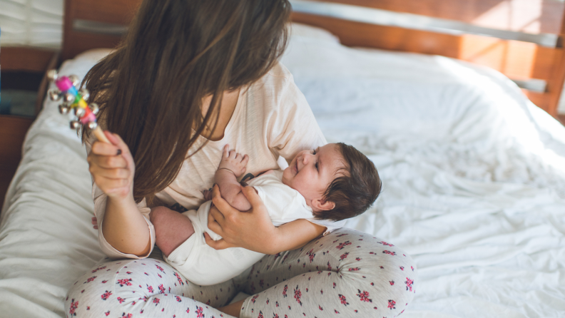 Mother is holding a baby girl and playing with a rattle