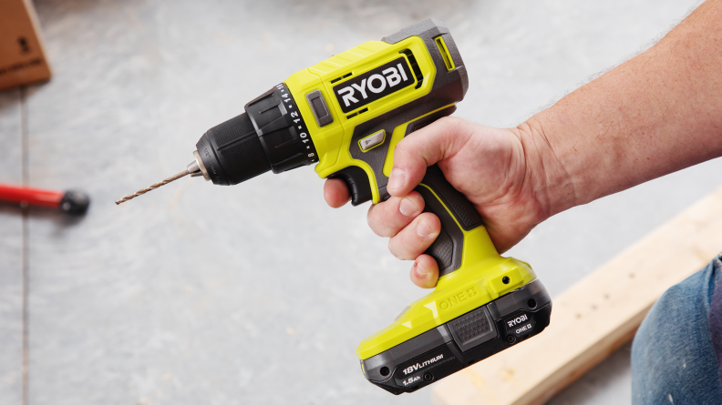 A hand holding a green Ryobi cordless drill and using it in a workshop
