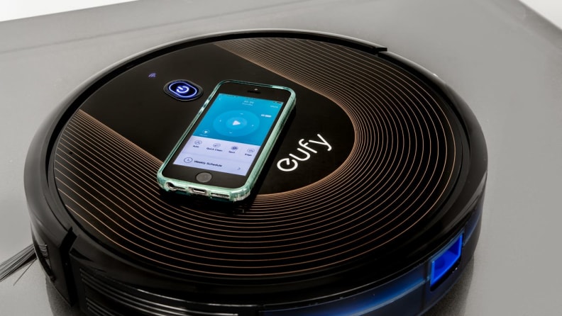 Black robot vacuum by Eufy with smart phone resting on top