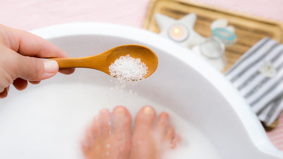 A woman pouring Epsom salt into a foot tub.