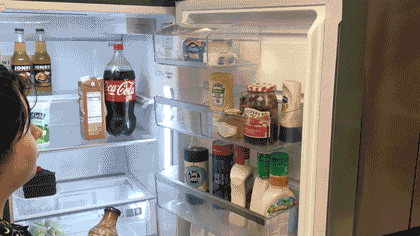 A person moving a shelf inside of the fridge and placing a bottle inside the shelf.