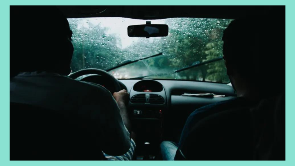Dark car interior as a driver and passenger navigate a heavy rainstorm. Wiper blades glide across the windshield in mid-motion.