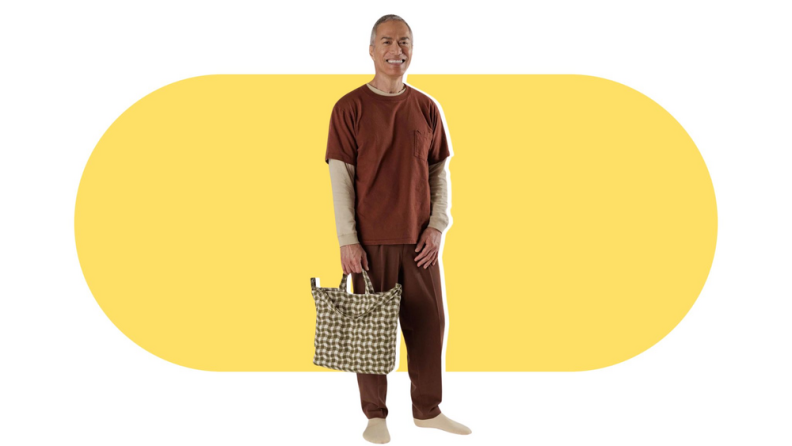 A male model holding a brown wavy-checked tote bag.