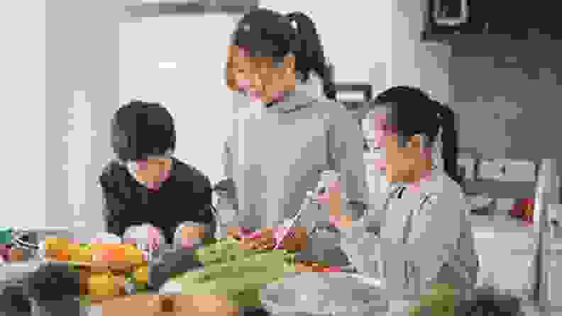 A parent prepares a meal with the help of their two children.