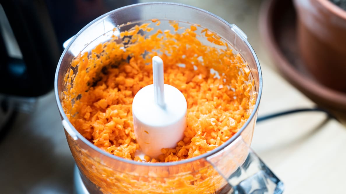 一台Cuisinart微型食品加工机，盖上盖子，在碗里切碎胡萝卜。