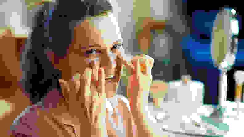 A woman applying eye cream to her face.