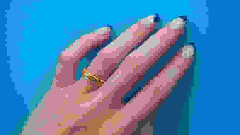 Woman's hand wearing gold ring set on blue background