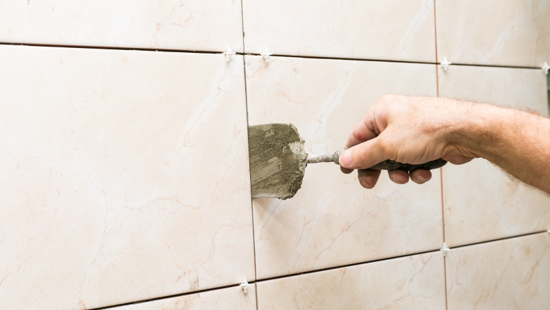 A person grouts a tile wall.