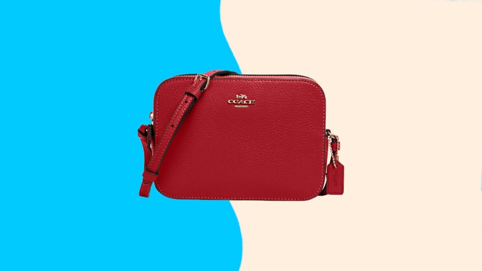 Red leather crossbody purse in front of cream and blue background.