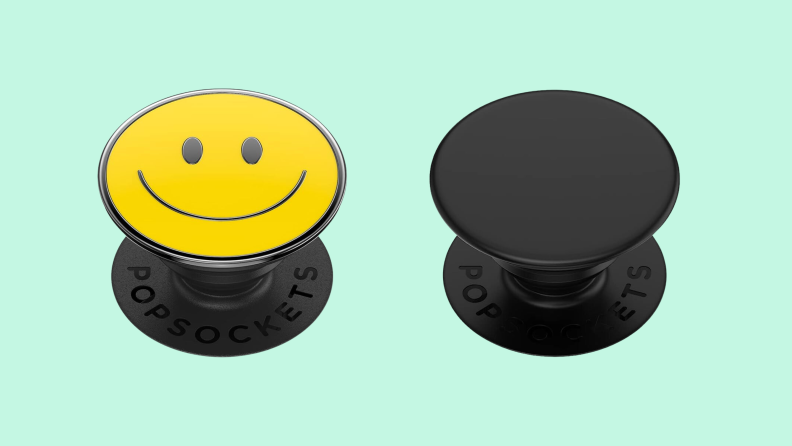A yellow smiley face PopSocket and a black PopSocket side-by-side on a light green background.