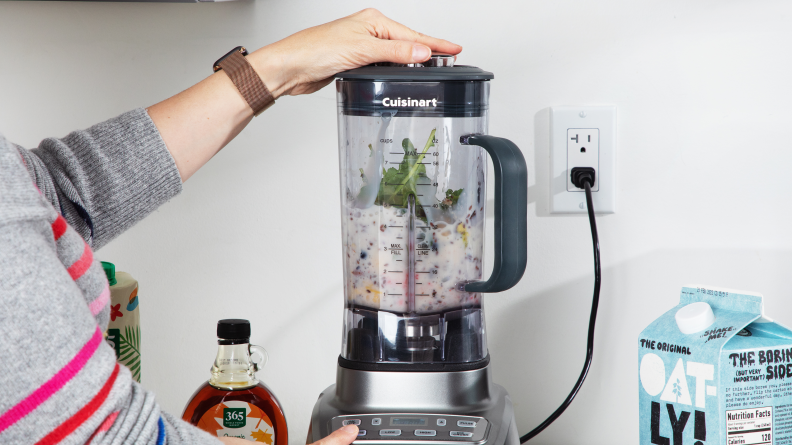 A person operates the Cuisinart Hurricane blender, which has smoothie ingredients inside.