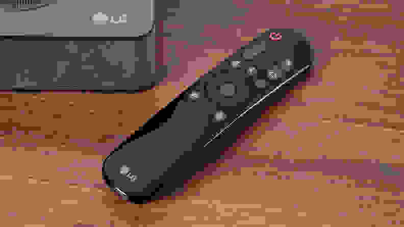 A remote control for an LG S80QY sits on a TV stand.