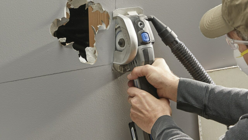 一个人用德梅尔US20V Ultra-Saw在墙上凿了一个洞。