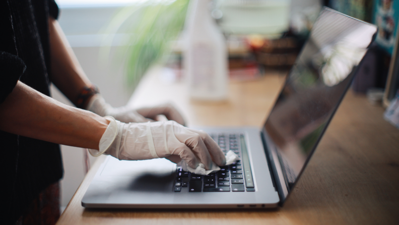 A woman sanitizes her laptop surface against viruses and germs.