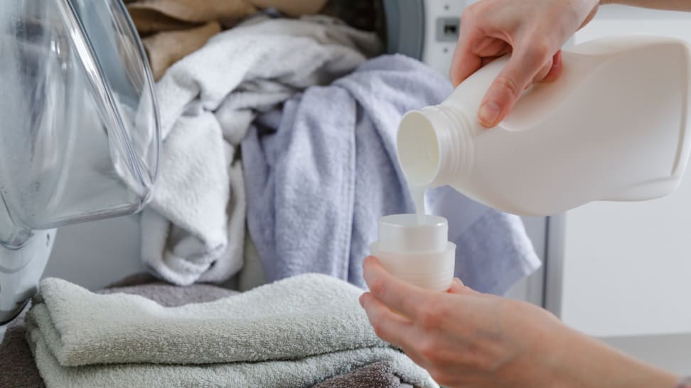 Hands pouring laundry detergent from bottle into cap