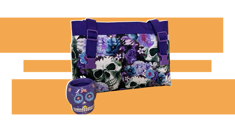 A purple bag with a skull and floral design sits next to a purple calavra mug from moBellaBags in front of an orange and white design.
