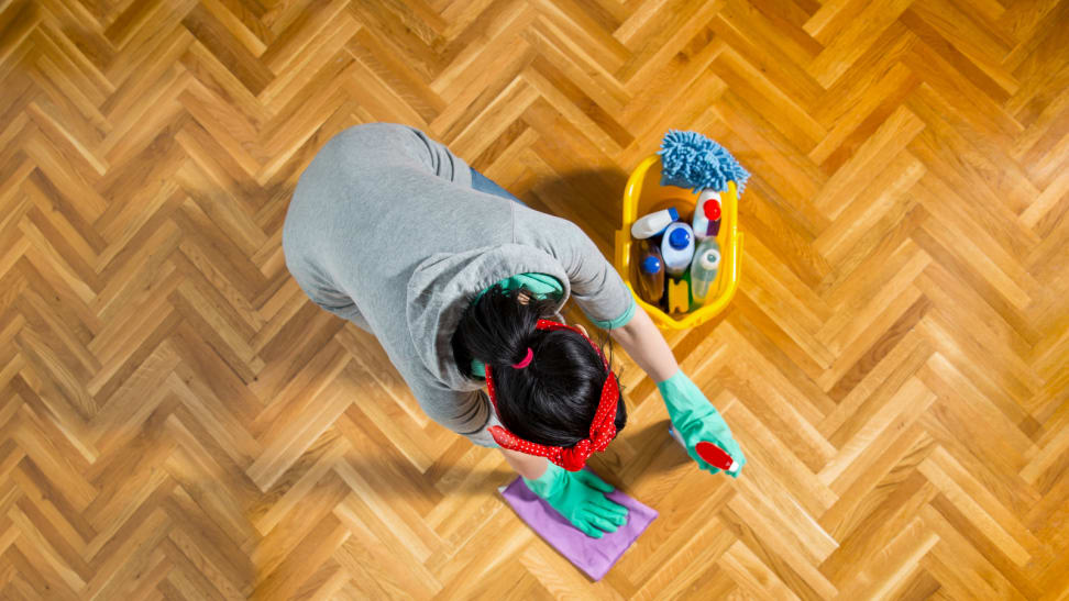 A woman cleans a hardwood floor on her knees