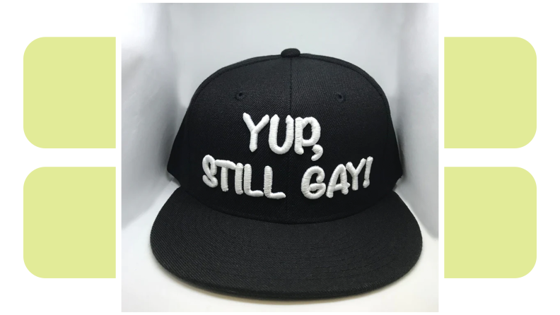 A black baseball cap that is embroidered with the words “Yup, still gay.”