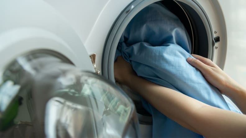 a person puts sheets into a washing machine