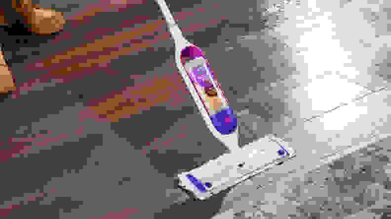 The Swiffer PowerMop mopping a wood floor next to an area rug.