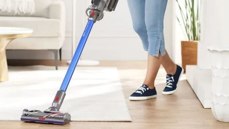 A person vacuums a carpet and wood floor with a Dyson vacuum.