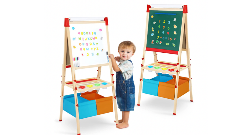 A child stands by two easels, one with a white board and one with a chalk board.