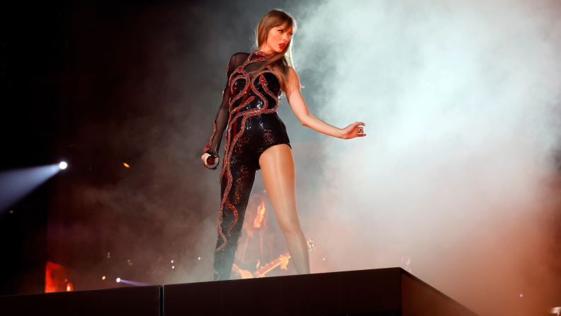 A photograph of Taylor Swift performing on stage, wearing a black and red jumpsuit.