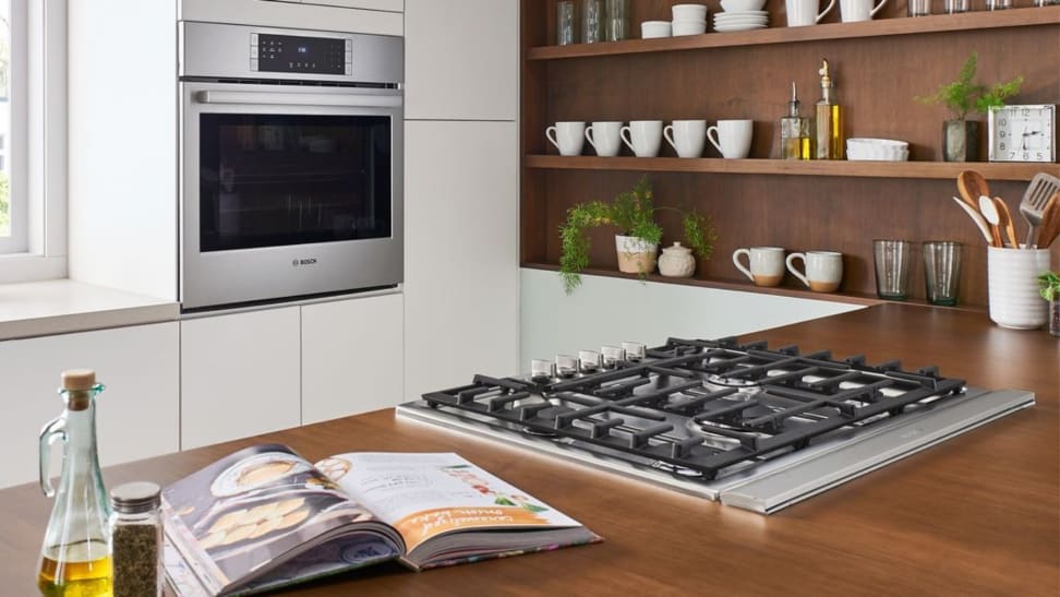 A lifestyle image of a gas cooktop and a corresponding wall oven in a brightly lit modern kitchen.